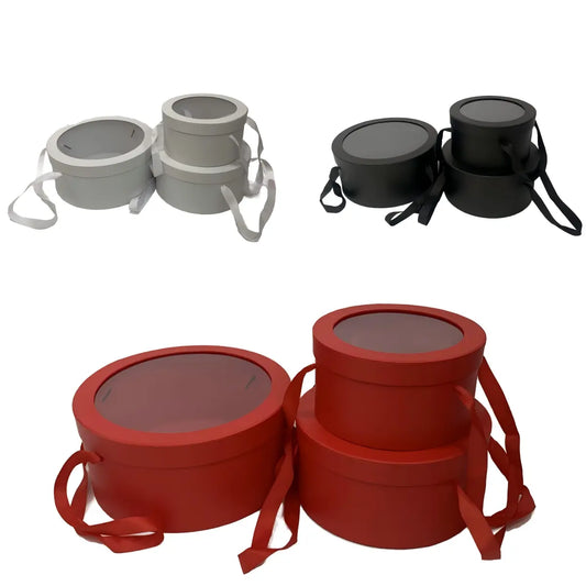 Round gift boxes with transparent lids and ribbon handles in red, pink, white, and black.
