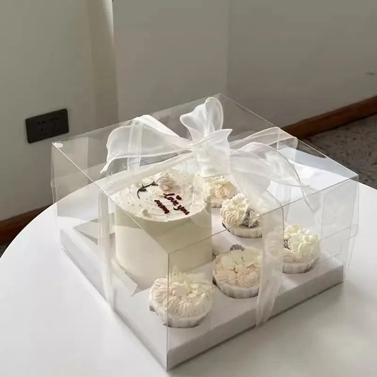 Clear cake and cupcake gift box with white ribbon, elegant bakery packaging.