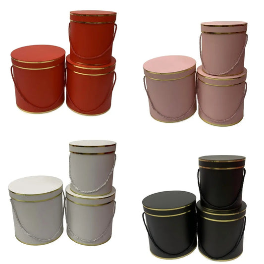 Round flower gift boxes with rope handles and gold trim in assorted colors.